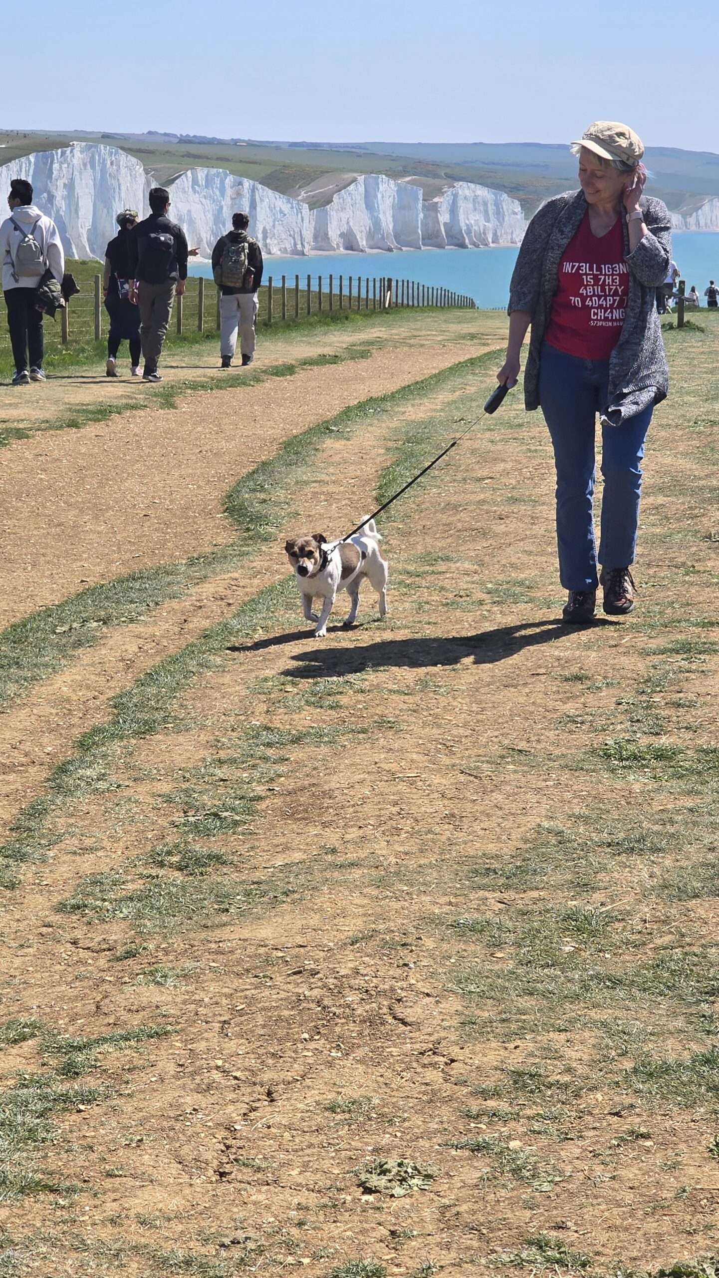 Woman walking a small dog on a coastal path overlooking white cliffs in East Sussex